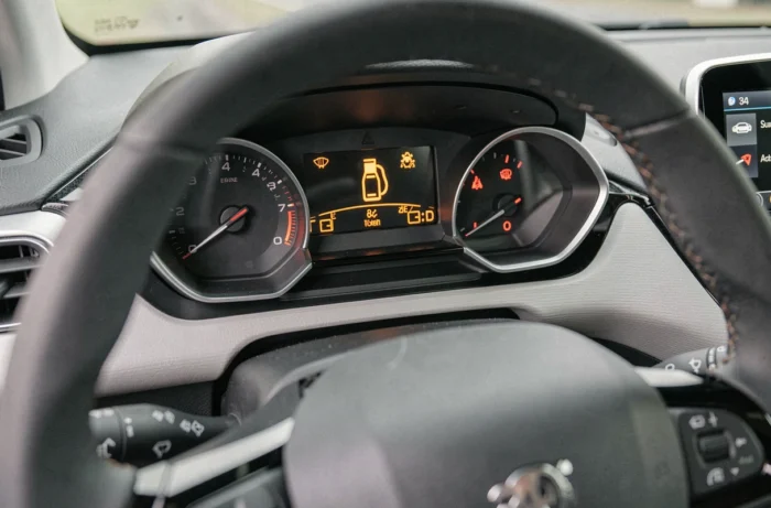 Tableau de bord d'une Peugeot 208 avec voyants lumineux allumés en orange et rouge indiquant des alertes moteur et batterie